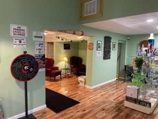 This photo is taken from The Joint Premium Dispensary store. This features The Joint's Sunday Fun Day wheel, a portion of the shelf with products on them, and a view of the smoking lounge.
